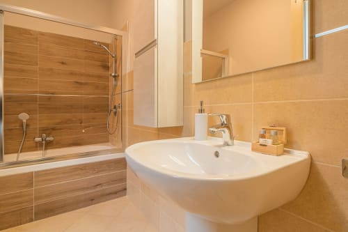 Bagno moderno presso Le Alpi bed & living con lavabo bianco curvo, doccia con rivestimento in legno, specchio e pareti color crema in Camera