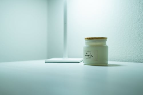 Dettaglio camera da letto Le Alpi: candela verde salvia Wild Meadow su scrivania bianca con arredamento minimalista e luminoso