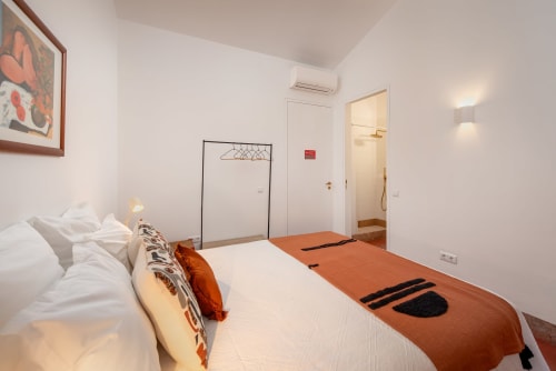 Quarto moderno em Monte das Açoteias com cama branca, manta laranja, assoalho de madeira e casa de banho privativa em Tavira, Portugal