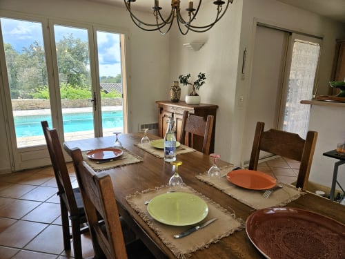 Salle à manger avec table en bois, couverts dressés et portes vitrées donnant sur la piscine bleue de la Villa Les Cyprès