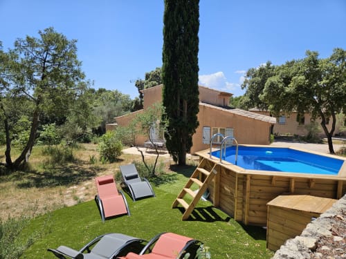 Jardin ensoleillé de villa avec piscine hors-sol, transats, cyprès et maison en terre cuite au Domaine de L'Échappée Belle
