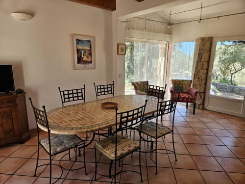 Dining room with oval mosaic table, black chairs, terracotta tiles, large windows overlooking gardens at Villa Les Oliviers,