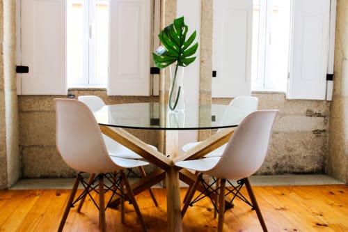 Área de jantar moderna do Bom Porto Apartments com mesa redonda de vidro, cadeiras rosa e decoração com planta monstera