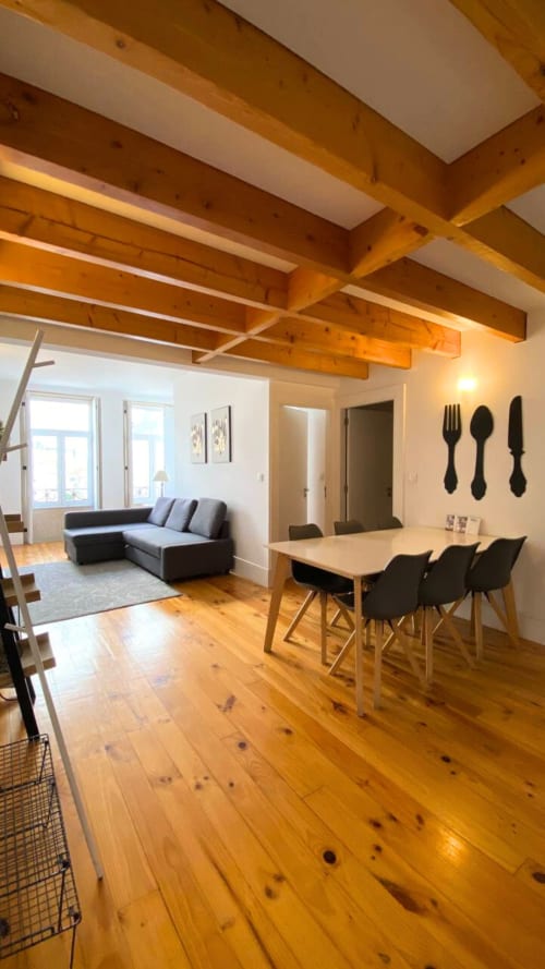 Moderno apartamento duplex no Porto com vigas de madeira, mesa de jantar, cadeiras pretas, sofá cinzento e soalho de madeira