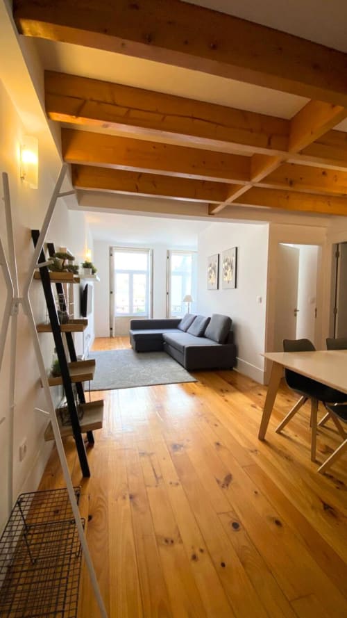 Interior moderno do apartamento duplex no Bom Porto Apartments com vigas de madeira aparentes, sofá preto, área de refeições e acabamentos em madeira