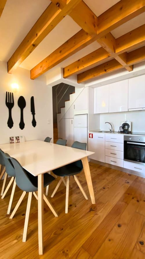 Sala de estar e cozinha moderna em apartamento no Porto com vigas de madeira aparentes, móveis brancos, mesa de refeições e piso em madeira.
