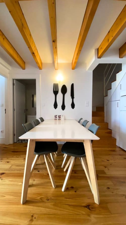 Sala de jantar moderna no Bom Porto Apartments com mesa branca, cadeiras pretas, vigas de madeira e arte de parede com garfo, faca e colher.