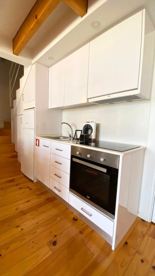 Cozinha moderna branca com forno embutido, cooktop em aço inoxidável, armários superiores e piso em madeira nos Apartamentos Bom Porto