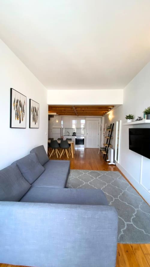 Sala de estar moderna em apartamento no Porto com sofá cinza, assoalho de madeira, TV e vista para a cozinha aberta