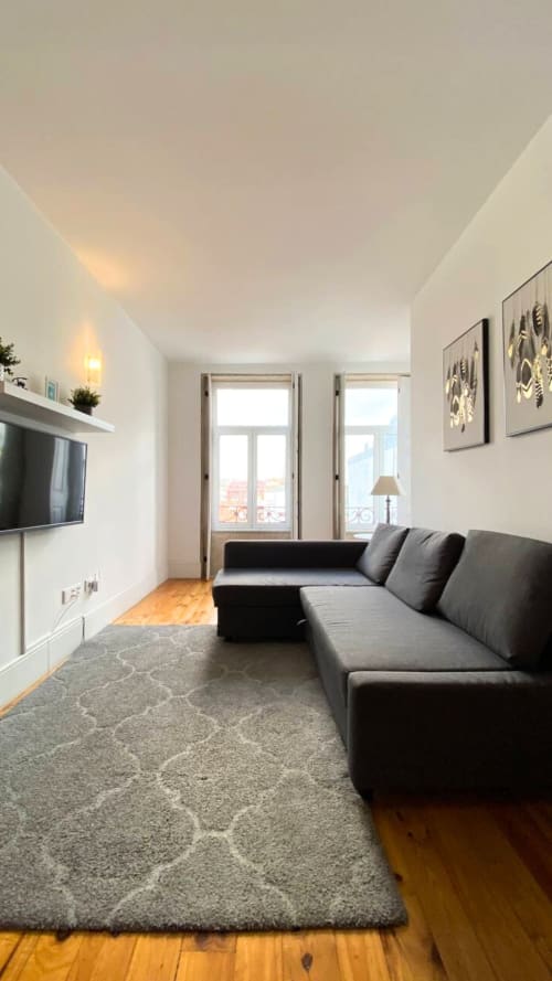Sala de estar moderna com sofá cinzento, TV na parede, pavimento em madeira e vista para a cidade no duplex Bom Porto Apartments no Porto