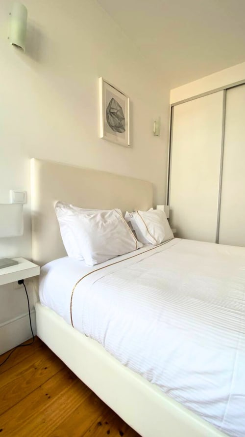 Quarto moderno e luminoso no Bom Porto Apartments com cama creme, roupa de cama branca, arte em folhas, piso de madeira e porta deslizante