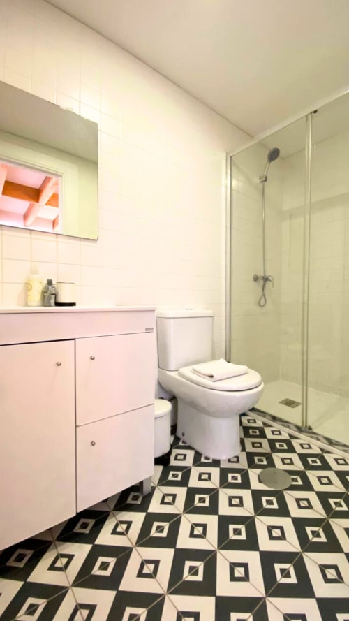Banheiro moderno em apartamento no Porto com penteadeira rosa, sanitário branco, piso xadrez preto e branco, e chuveiro de vidro