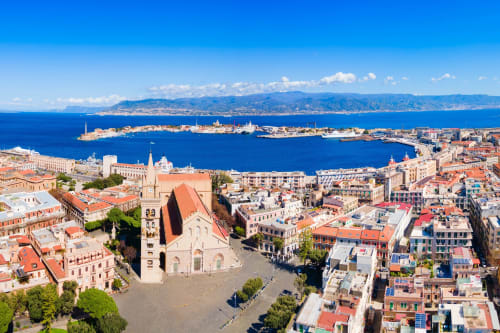 Vista aerea di Messina con edifici colorati, chiesa e il blu Mar Mediterraneo con la costa della Calabria sullo sfondo