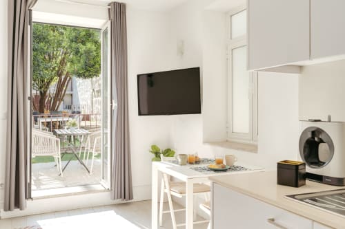 Cozinha e zona de refeições de apartamento T1 moderno no Porto com vista para o jardim através de portas de terraço abertas, TV de ecrã plano, e