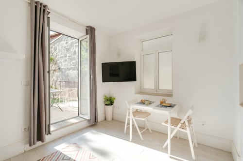 Apartamento T1 luminoso em Bom Porto com sala de refeições, TV, mobiliário branco, acesso a terraço com vista para jardim, Porto