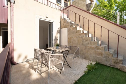 Terraço ensolarado do Bom Porto Apartments com mesa de jantar, cadeiras, escadas de pedra e vista para o jardim no Porto