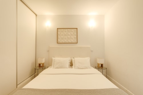 Quarto minimalista luminoso no Bom Porto Apartments com cama queen, roupas de cama brancas, mesas lateral e arte na parede