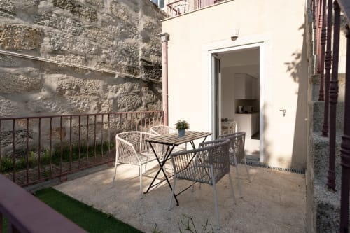 Terraço ensolarado do Bom Porto Apartments com mesa de refeições, cadeiras de vime e paredes em pedra no Porto