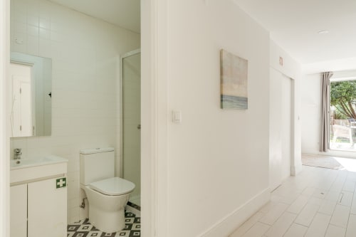 Banheiro e corredor modernos do Bom Porto Apartments, Porto, com azulejos brancos, espelho, vaso sanitário e vista para a sala de estar