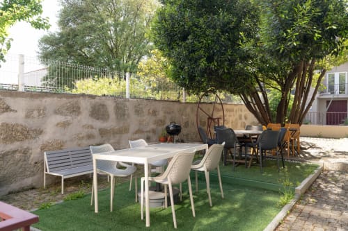 Terraço exterior do Bom Porto Apartments no Porto com mesas de refeição, cadeiras brancas, árvores frondosas e muros de pedra