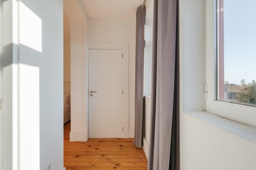 Corredor moderno no Bom Porto Apartments Porto com piso em madeira, porta branca e vistas para o jardim através de grande janela