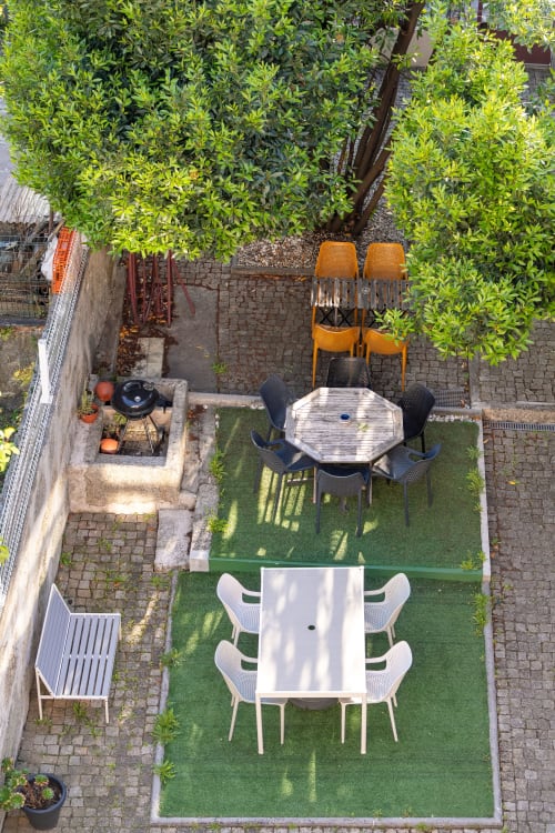 Vista aérea do pátio-jardim do Bom Porto Apartments com mesas de jantar, vegetação exuberante e áreas de estar no Porto.