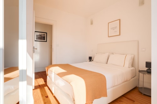 Quarto luminoso nos Apartamentos Bom Porto com cama queen, roupa de cama creme, piso de madeira e vista para o jardim pela janela no Porto