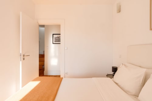 Quarto luminoso no Bom Porto Apartments com cama, portas brancas, piso em madeira e vista para o jardim no Porto