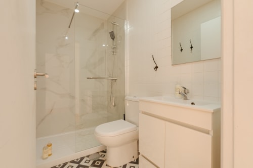 Banheiro moderno do Bom Porto Apartments com box de vidro, vaso branco, pia com gabinete e piso com azulejos geométricos