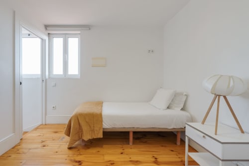 Quarto luminoso nos Apartamentos Bom Porto com cama individual, piso de madeira e vista para o jardim pelas portas do Porto