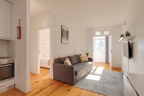 Sala de estar moderna em apartamento no Porto com sofá cinzento, soalho em madeira, cozinha integrada e portas com vista para o jardim