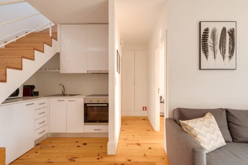 Apartamento duplex de planta aberta no Porto com escadas de madeira, cozinha branca e sofá cinzento com vista para jardim