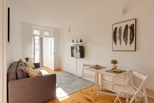 Área de estar clara no Bom Porto Apartments com sofá marrom, mesa de jantar em madeira, TV, quadro de samambaia e vista para o jardim