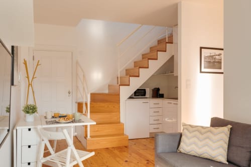 Estúdio duplex no Bom Porto em Porto com escadas em madeira, cozinha branca, área de jantar e sofá com vista para o jardim