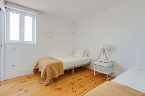 Quarto luminoso no Bom Porto Apartments no Porto com piso de madeira, cama individual com manta amarela, criado branco com luminária