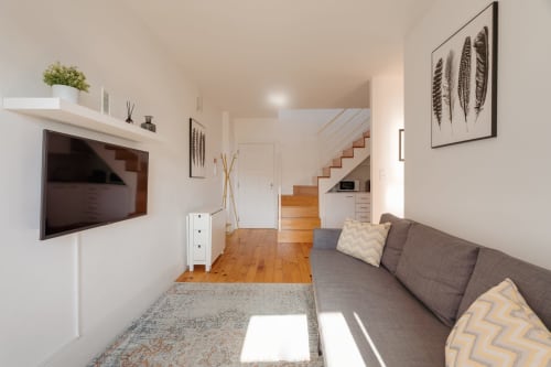 Sala de estar moderna do apartamento tipo duplex com sofá cinzento, televisão, escadas de madeira e vista para o jardim nos Apartamentos Bom Porto, Porto