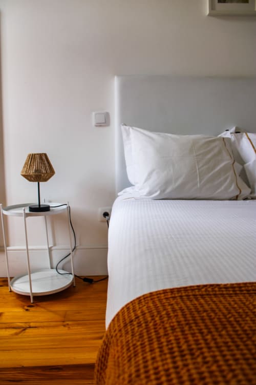 Quarto moderno no Bom Porto Apartments com roupa de cama branca, criado de madeira com luminária trançada e piso em madeira no Porto.