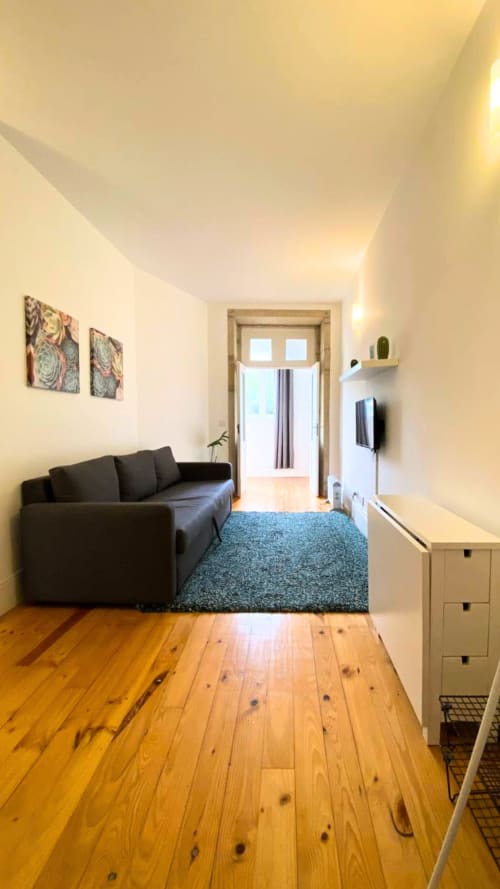 Sala de estar moderna em apartamento do Porto com sofá preto, piso de madeira e porta com vista para o jardim