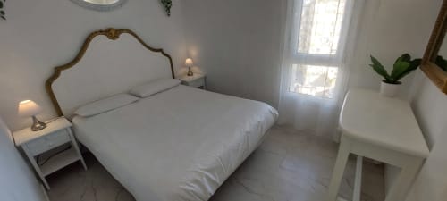Dormitorio luminoso con vista al mar en VIVE Benalmádena, ropa de cama blanca, cabecero ornamentado y muebles modernos