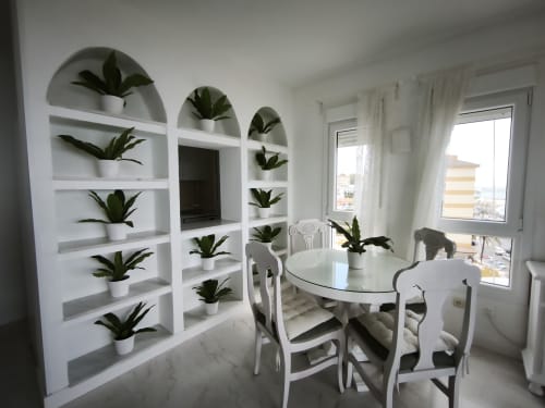 Comedor moderno con mesa redonda blanca, sillas y estanterías arqueadas con plantas en maceta en la costa de Benalmádena