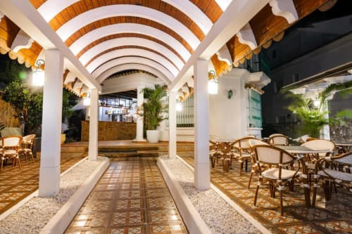 Terraza cubierta elegante del Hotel Boutique Zahara con arcos de ladrillo, mesas de comedor y plantas tropicales en Cádiz
