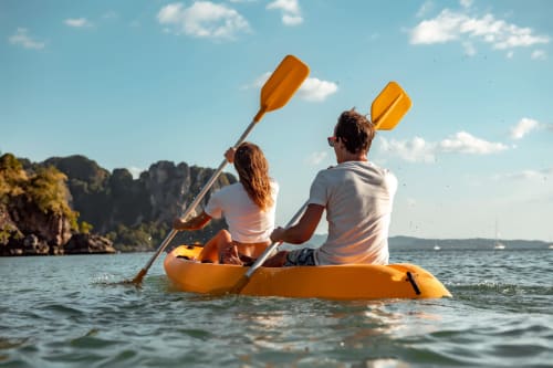 Pareja navegando en kayak amarillo frente a la playa de Zahara de los Atunes con acantilados rocosos y veleros a la vista