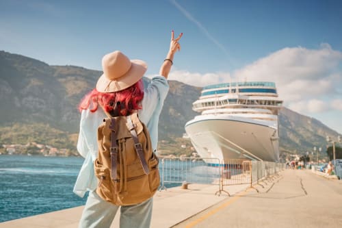 Viajera pelirroja con mochila celebrando en el puerto de Zahara de los Atunes con crucero atracado