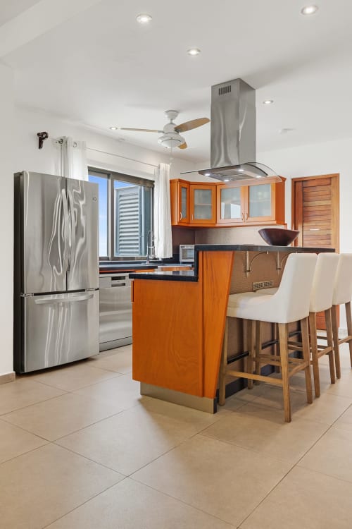 Modern kitchen with orange cabinetry, stainless steel appliances, island seating, and ceiling fan at Isla Mujeres villa.