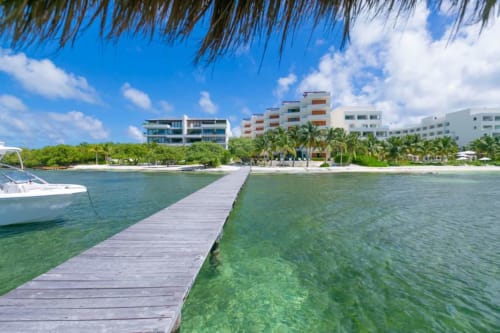 Wooden dock extending into turquoise waters with beachfront condos and palm trees at Isla Mujeres resort in Mexico