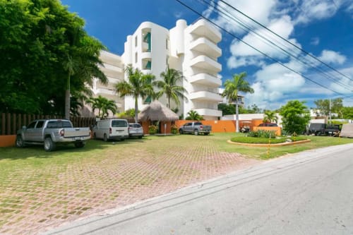 Modern white beachfront condo building in Isla Mujeres with tropical grounds, parking, and sea views