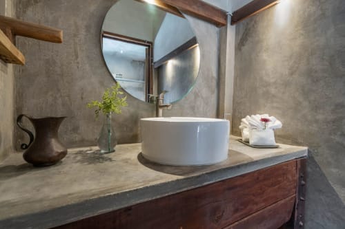 Modern bathroom at Aruma Boutique Isla Mujeres villa with round white sink, circular mirror, stone countertop, and dark wood