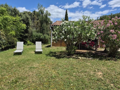 Two white lounge chairs on grass with flowering shrubs and countryside views at Domaine en Terre Happy, Labastide-de-Virac