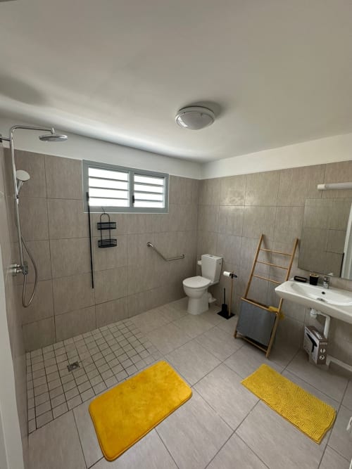 Salle de bains moderne au Maly Blue Location à Le Moule avec douche à l'italienne, toilettes, lavabo, tapis de bain jaunes et fenêtre