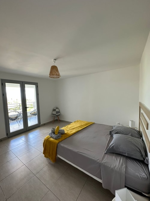Chambre moderne à Maly Blue Location au Moule avec balcon, lit queen-size, touches jaunes et luminaire tressé au plafond